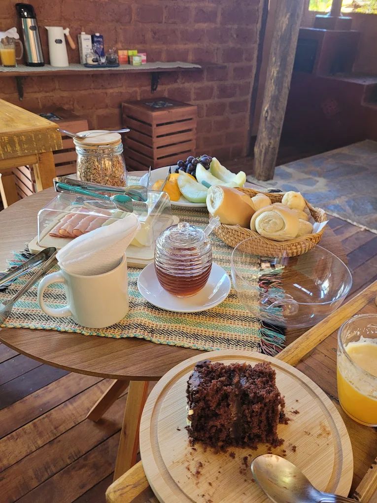 Mesa redonda com bolo de chocolate, mel, frutas e pães